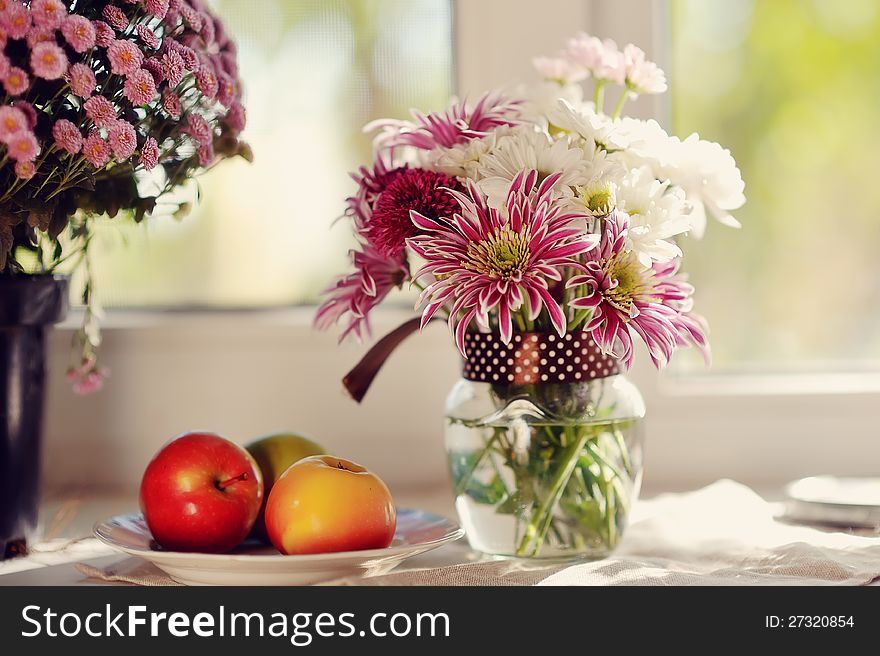 On a white plate ripe apples and bright bouquet of autumn flowers. On a white plate ripe apples and bright bouquet of autumn flowers