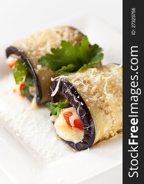 Eggplant rolls with vegetables and cheese on a white plate