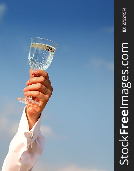 A glass of water held up in a toast against a bright cloudy blue sky background. A glass of water held up in a toast against a bright cloudy blue sky background