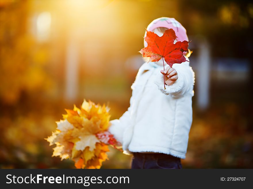 Small girl hiding her face with maple leaf outdoor