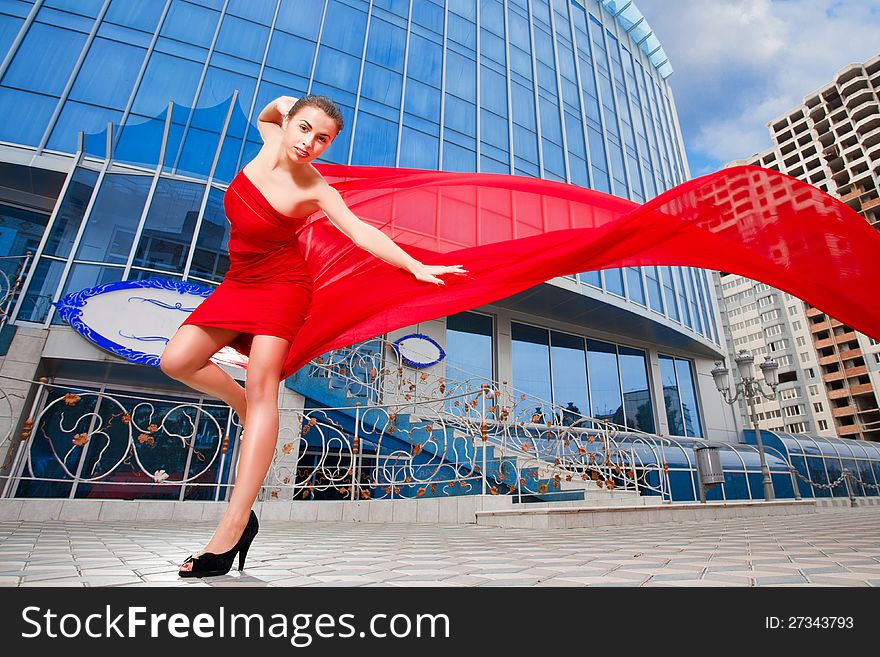 Young beautiful girl with the red flying fabric in the city