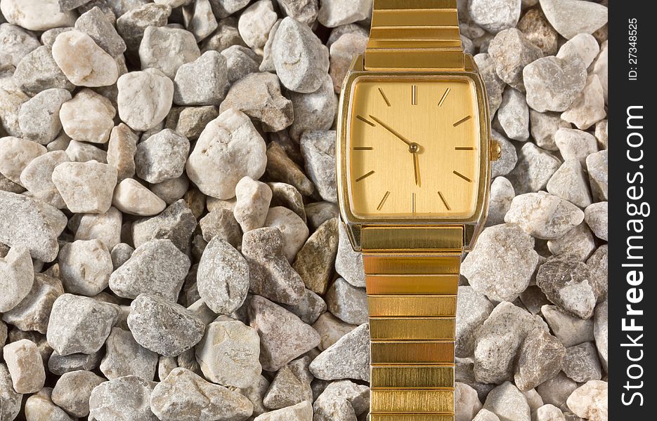 False gold wristwatch on a gravel background. False gold wristwatch on a gravel background