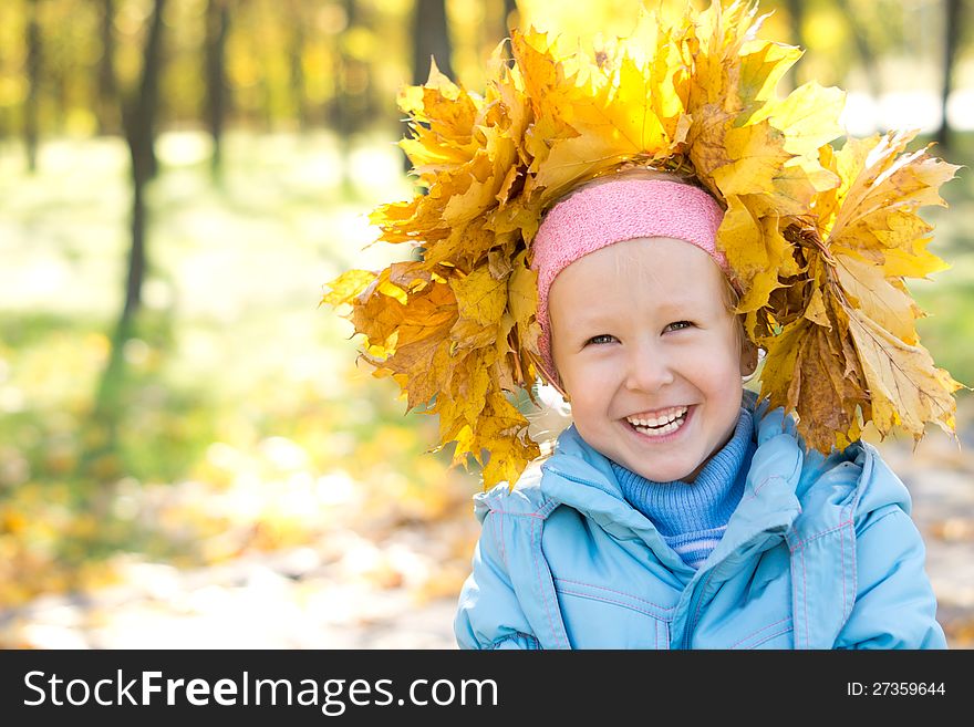 Laughing little girl wearing a hat fashioned from yellow autumn leaves that she has collected herself with copyspace. Laughing little girl wearing a hat fashioned from yellow autumn leaves that she has collected herself with copyspace