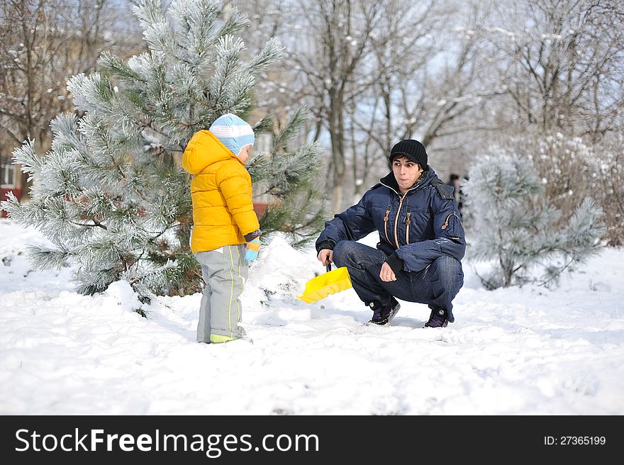 Winter child in a yellow jacket with a men playing in the snow. Winter child in a yellow jacket with a men playing in the snow