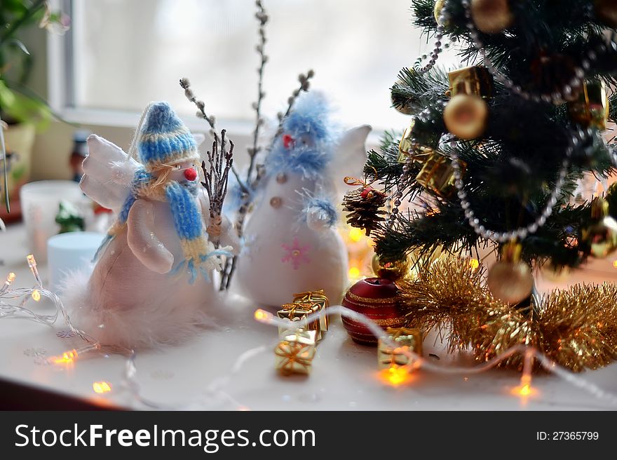 Near a Christmas tree decorated with lights and toys are two snowmen. Near a Christmas tree decorated with lights and toys are two snowmen