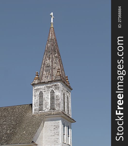 Old, worn, and weathered white wooden Christian church steeple with a cross on top. Isolated against a clear blue sky. Old, worn, and weathered white wooden Christian church steeple with a cross on top. Isolated against a clear blue sky.