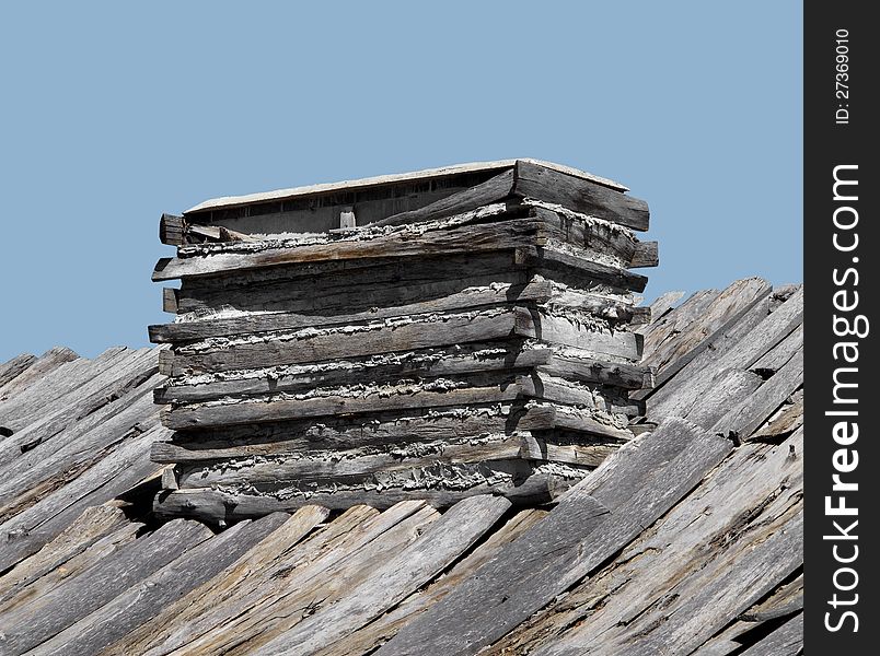 Close-up of a vintage fireplace chimney on a log cabin roof made from logs, wood, and caulked with mud.  Isolated against a blue sky. Close-up of a vintage fireplace chimney on a log cabin roof made from logs, wood, and caulked with mud.  Isolated against a blue sky.
