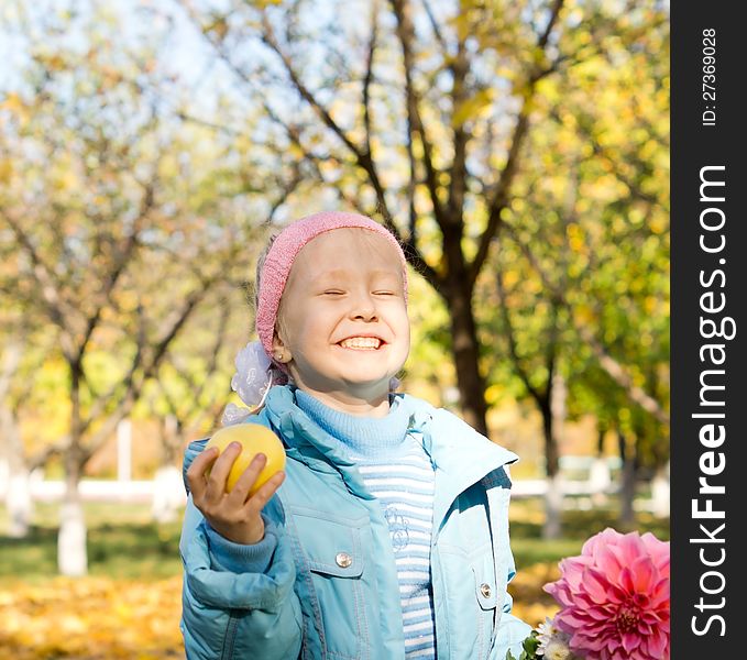 Little girl with a cheesy mischievous grin holding an apple and a fresh pink dahlia standing in colourful autumn countryside. Little girl with a cheesy mischievous grin holding an apple and a fresh pink dahlia standing in colourful autumn countryside