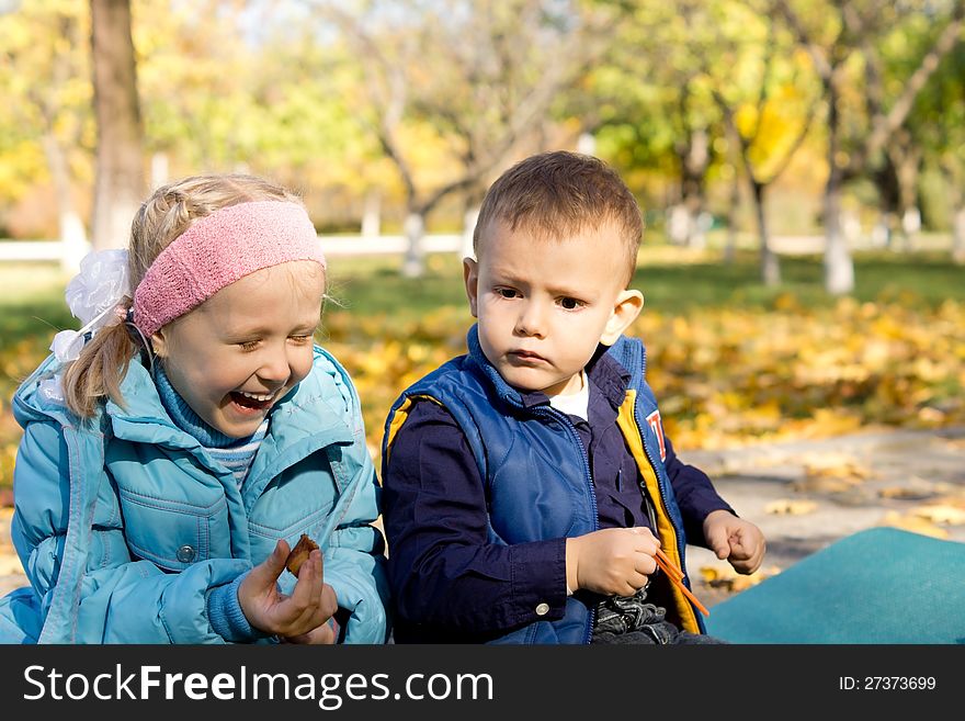 Young girl sitting by small boy laughing outside in beautiful autumn woodland. Young girl sitting by small boy laughing outside in beautiful autumn woodland