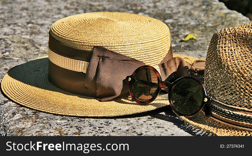 An elegant straw hat with ribbon and fashionable glasses laying on a old stone bench. An elegant straw hat with ribbon and fashionable glasses laying on a old stone bench.