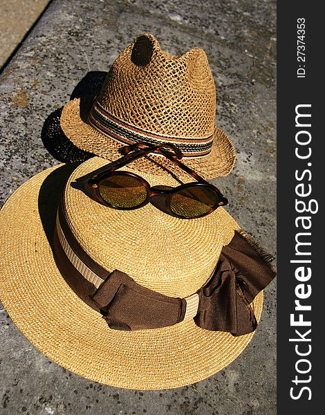 An elegant straw hat with ribbon and fashionable glasses laying on a old stone bench. An elegant straw hat with ribbon and fashionable glasses laying on a old stone bench.