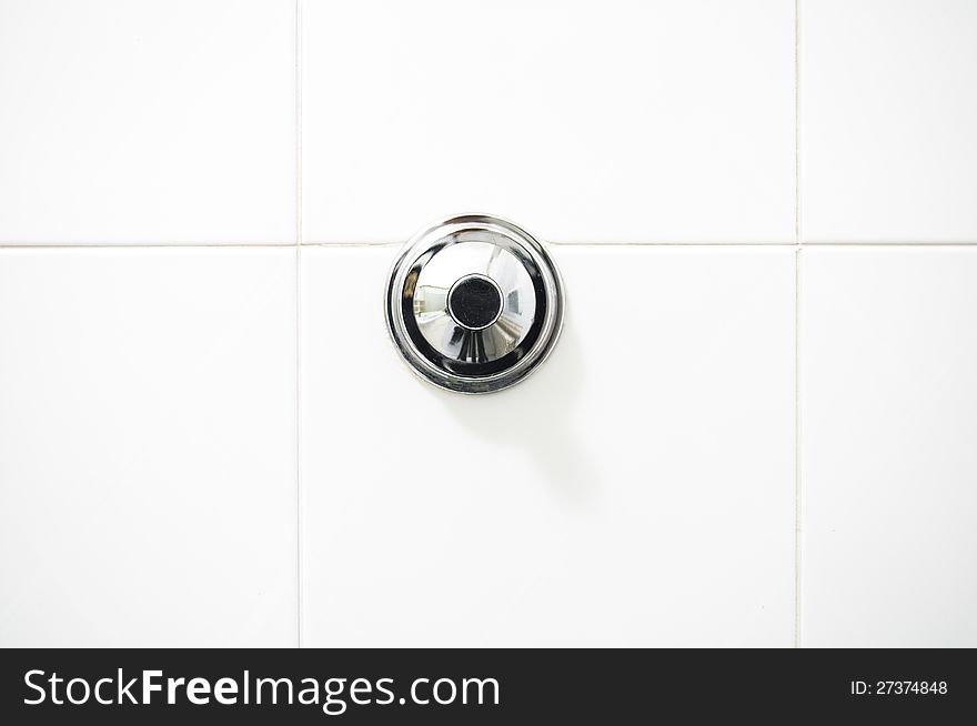 Chrome flush button on a white toilet against a white wall. Chrome flush button on a white toilet against a white wall.