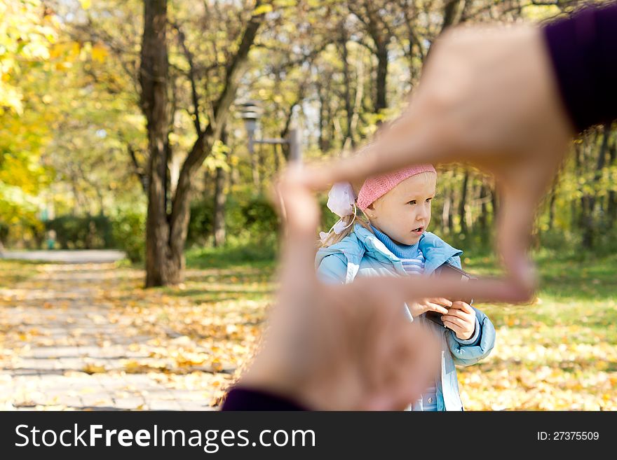 Little girl playing in a park seen through a finger frame framing her face. Little girl playing in a park seen through a finger frame framing her face