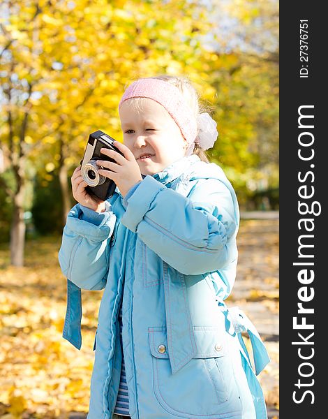 Aspiring young girl photographer trying to fathom out how to use a vintage slr camera as she stands outdoors in an autumn park