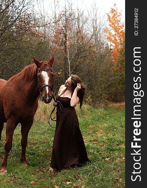 Pretty young woman in a long gown stands with her horse in Autumn. Pretty young woman in a long gown stands with her horse in Autumn.