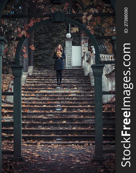 Girl stays on the stairs holding bunch of the leaves in her hands with arc on the foreground. Girl stays on the stairs holding bunch of the leaves in her hands with arc on the foreground