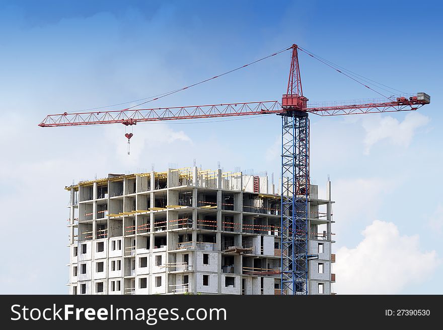 A tower crane and an unfinished building at a construction site against a blue sky background. A tower crane and an unfinished building at a construction site against a blue sky background