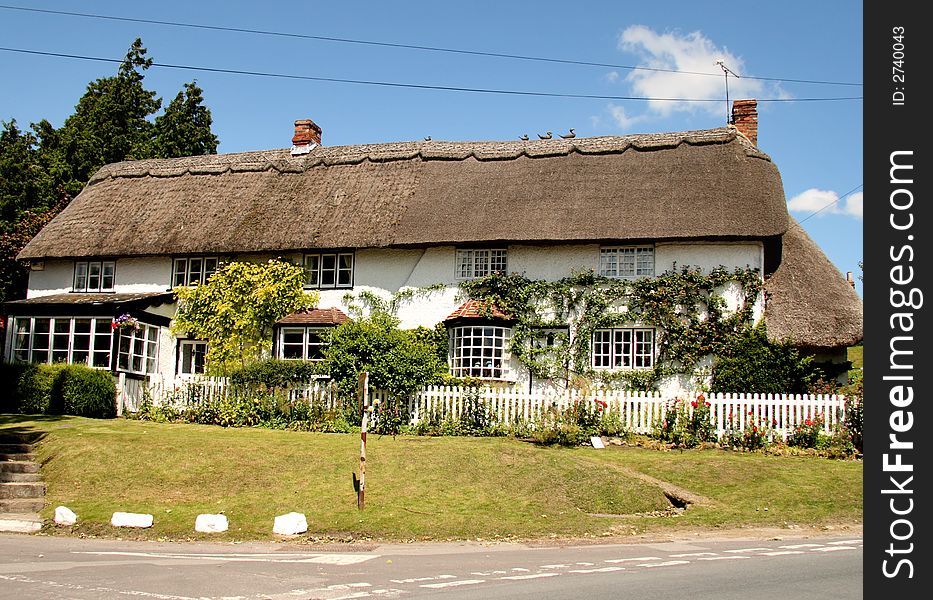 Thatched and whitewashed English Village House with picket fence in front and covered with climbing flowers. Thatched and whitewashed English Village House with picket fence in front and covered with climbing flowers