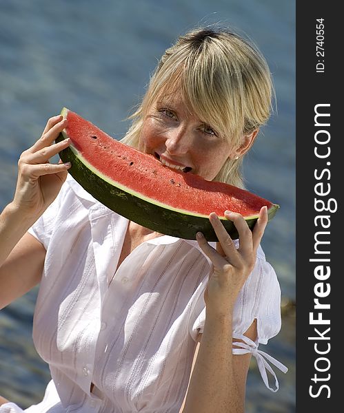 Young blonde girl eating watermelon by the sea