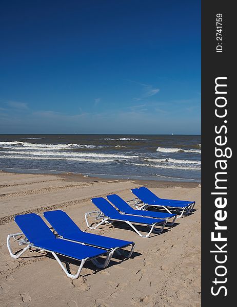 Six blue beach chairs in the sand with the sea/ocean on the background, plenty of copyspace. Six blue beach chairs in the sand with the sea/ocean on the background, plenty of copyspace