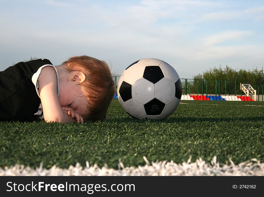 The boy lays on an artificial covering of stadium near to a ball. The boy lays on an artificial covering of stadium near to a ball