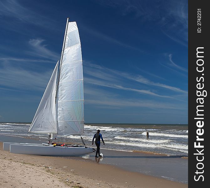 A catamaran sail boat at the beach with white sail and beautiful blue sky and some white clouds. A catamaran sail boat at the beach with white sail and beautiful blue sky and some white clouds.