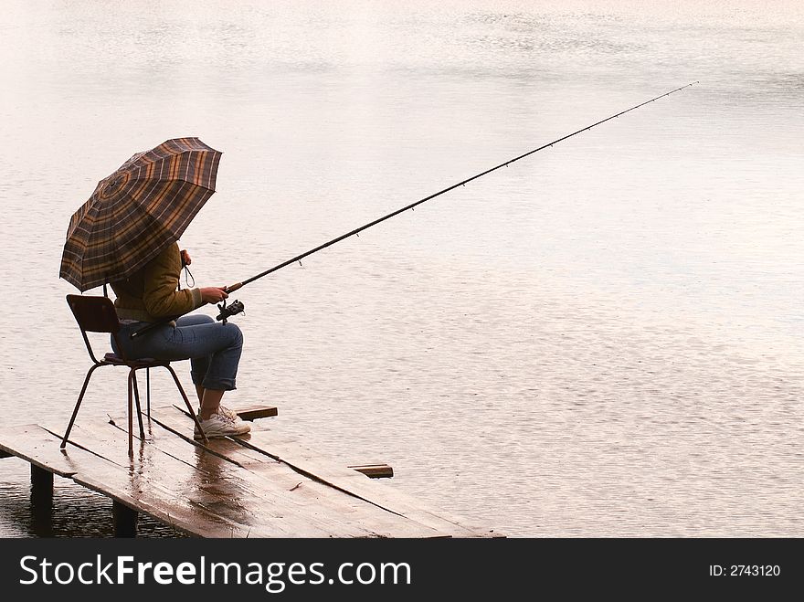 The woman fishes on lake under a rain. The woman fishes on lake under a rain