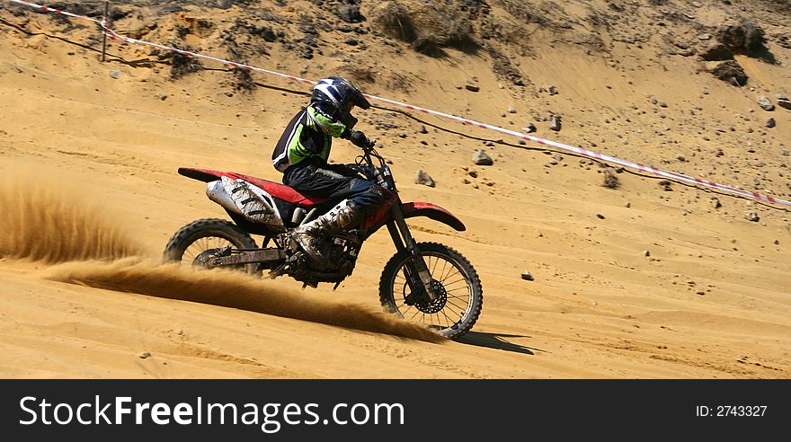 The sportsman on a motorcycle overcomes abrupt turn on a sandy line. The sportsman on a motorcycle overcomes abrupt turn on a sandy line