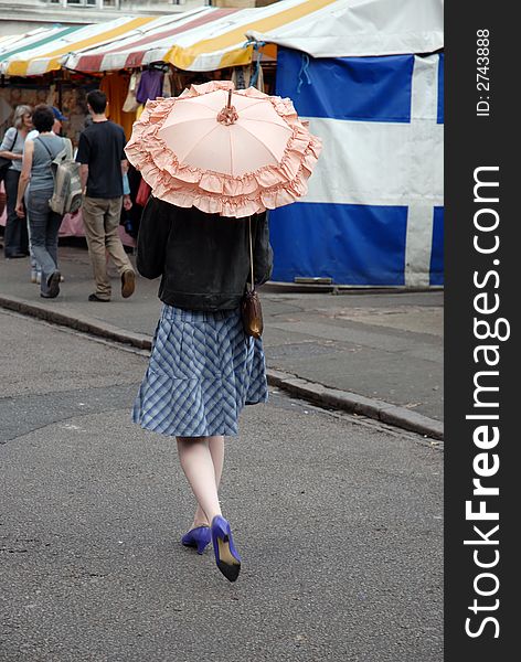 Woman walks through market shaded by pink parasol. Woman walks through market shaded by pink parasol.