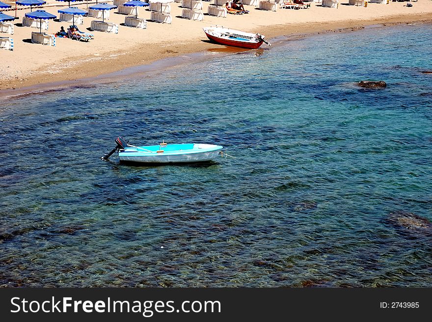 Small sandy beach, little harbour with motorboats, beach chairs and umbrella. Sunny day. Rhodes, Greece. Small sandy beach, little harbour with motorboats, beach chairs and umbrella. Sunny day. Rhodes, Greece.