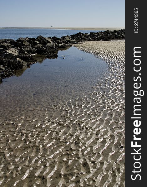 Sun lit ripples in the sand behind a jetty