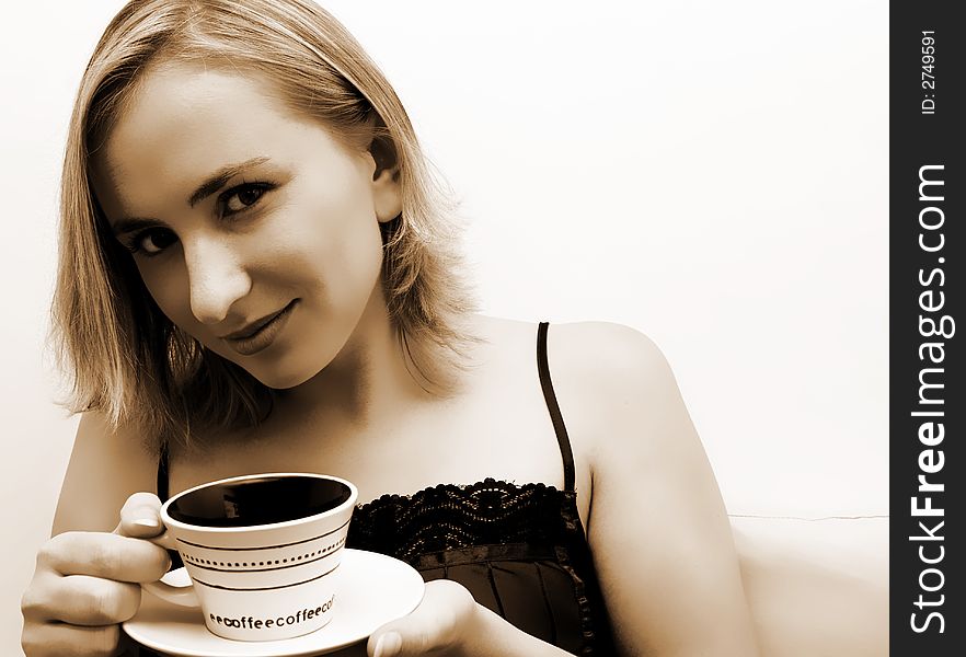 Beautiful blonde girl sitting on the bed in the morning, drinking her coffee