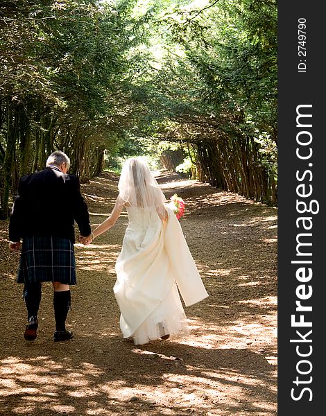 A bride & groom walking through a tree-lined avenue. A bride & groom walking through a tree-lined avenue