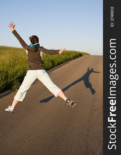 Woman from behind in sporty clothes. Cuts a caper - jumps into the air. Picture from behind with long shadow on the street. Woman from behind in sporty clothes. Cuts a caper - jumps into the air. Picture from behind with long shadow on the street.