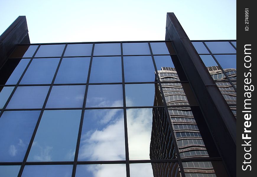 Clouds and an office building reflected in the mirrored windows of another office building with a pale blue sky above. Clouds and an office building reflected in the mirrored windows of another office building with a pale blue sky above.