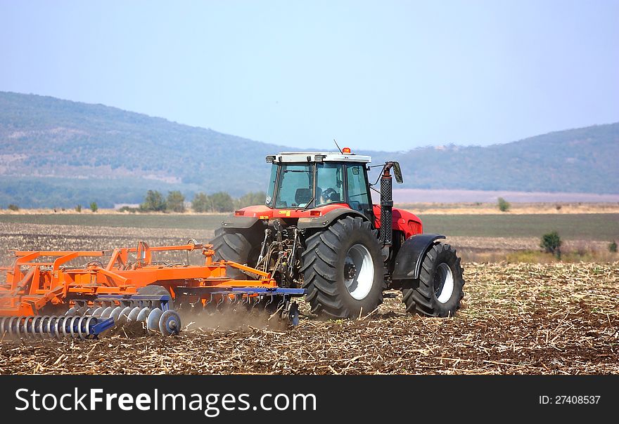 A tractor working outdoor in a field with mountain background. A tractor working outdoor in a field with mountain background