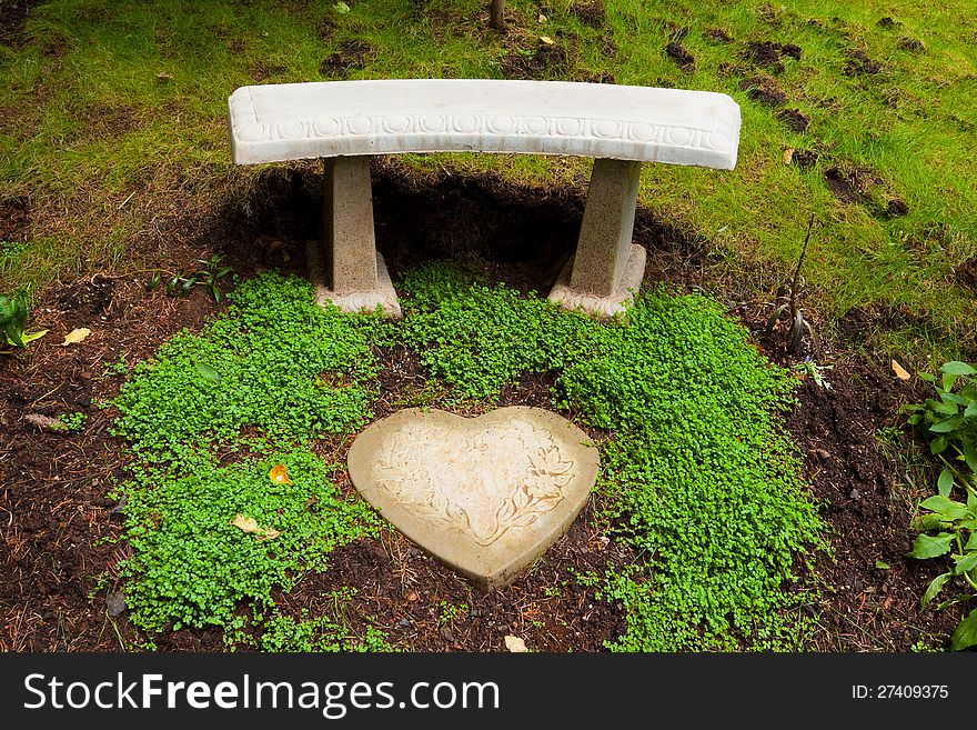 A beautiful stone bench sits next to some green clover and a heart shaped stone tile piece in a perfectly manicured garden in Oregon. A beautiful stone bench sits next to some green clover and a heart shaped stone tile piece in a perfectly manicured garden in Oregon.