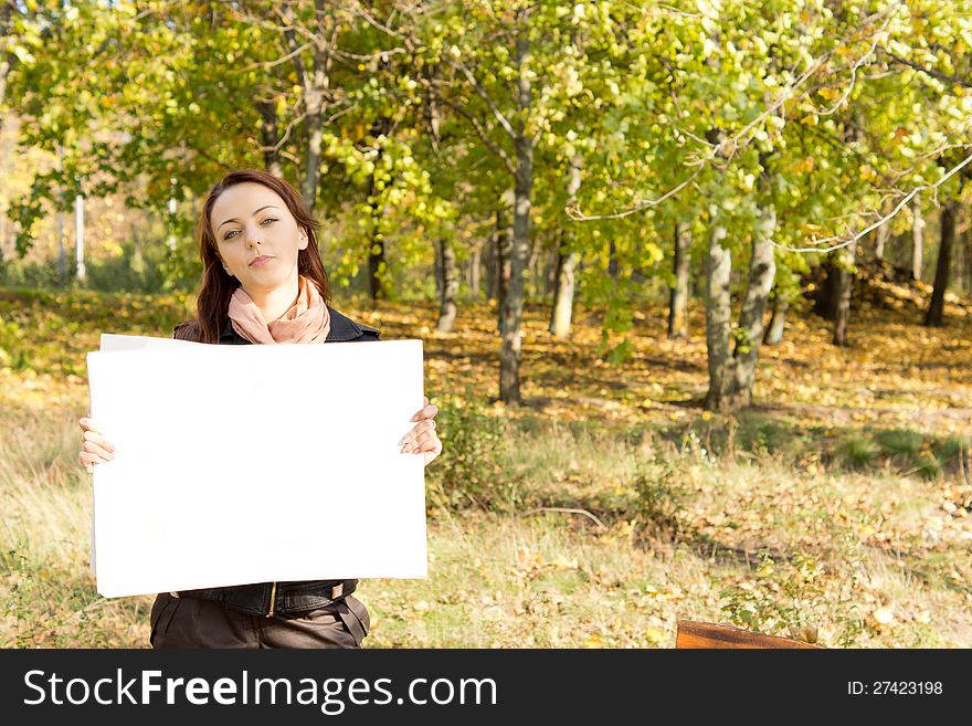 Attractive young woman standing in wooded countryside holding a blank white card for your text or advertisement. Attractive young woman standing in wooded countryside holding a blank white card for your text or advertisement