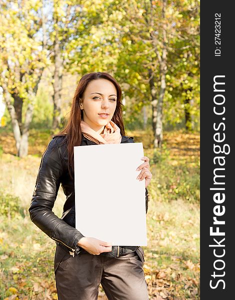 Beautiful trendy young woman holding a blank sign for your text in her hands standing outdoors in woodland. Beautiful trendy young woman holding a blank sign for your text in her hands standing outdoors in woodland