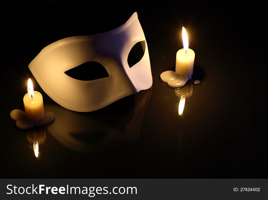 White mask between lighting candles on dark background. White mask between lighting candles on dark background