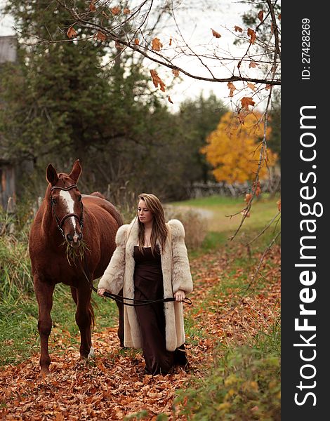Pretty young woman in a long gown and fur coat walking with her horse in Autumn. Pretty young woman in a long gown and fur coat walking with her horse in Autumn.