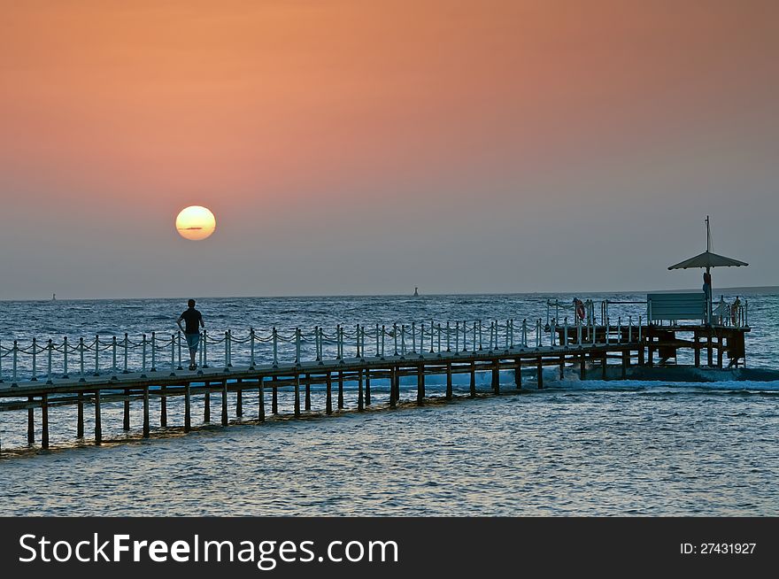 The person on a pier during sunrise on the sea