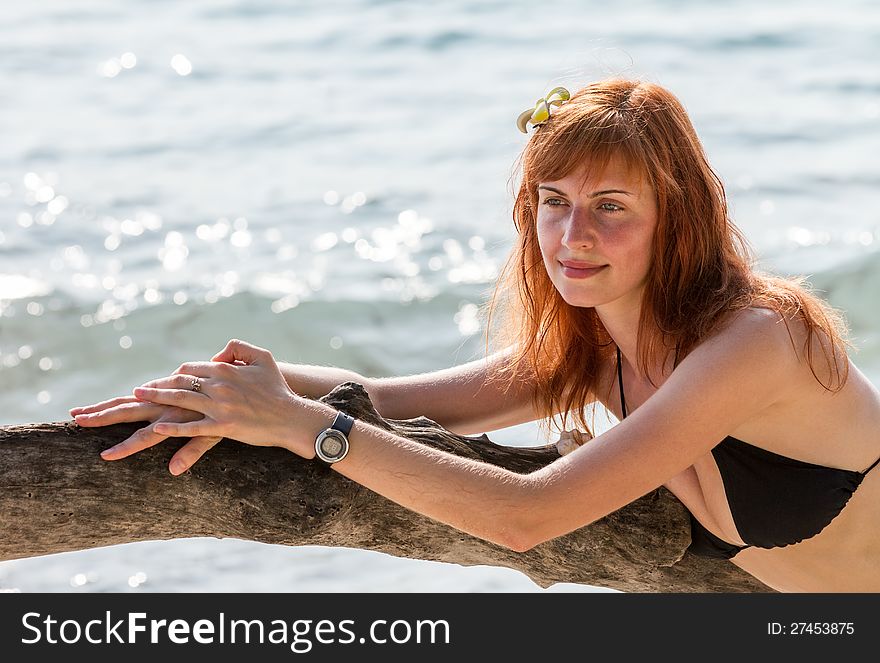 Young woman in bikini posing on branchy log in water