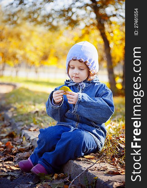 Little Curly Girl Sits In Autumn Park