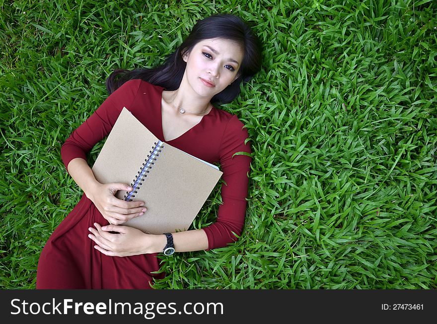 Woman lying on green grass with a book