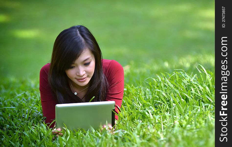 Pretty woman using tablet outdoor laying on grass