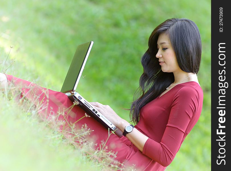 Pretty woman with laptop on green grass at the garden