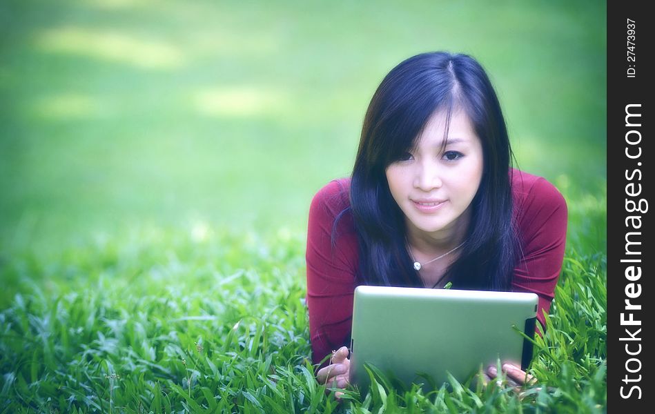 Pretty woman using tablet outdoor laying on grass