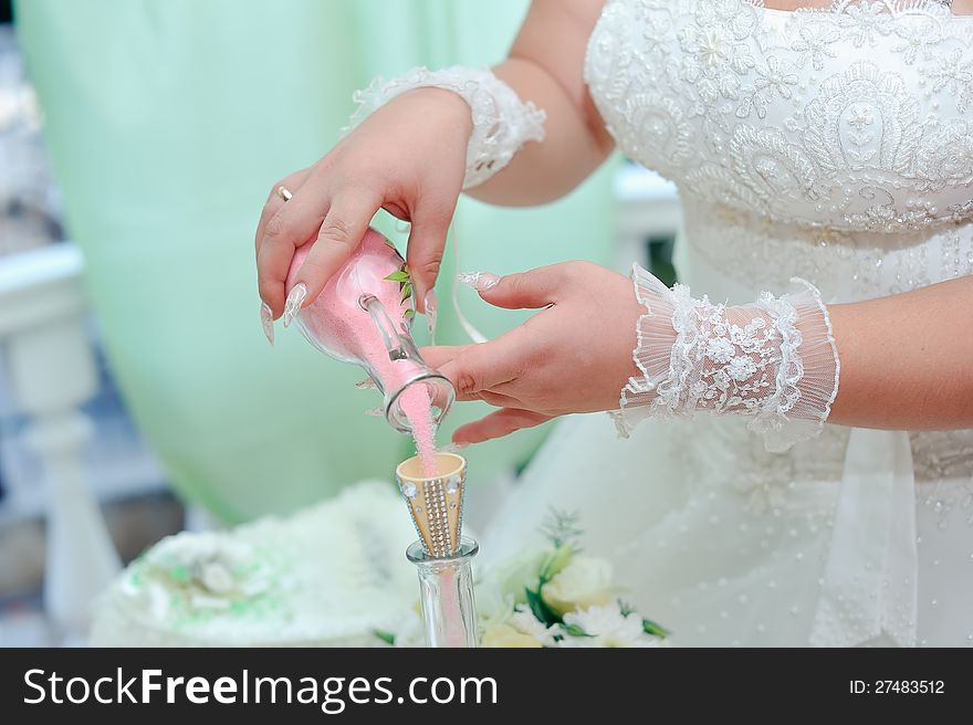 Beautiful bride's hands poured colored sand into a bottle. Beautiful bride's hands poured colored sand into a bottle