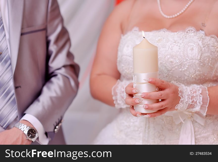 Beautiful bride's hands holding a large white candle. Beautiful bride's hands holding a large white candle